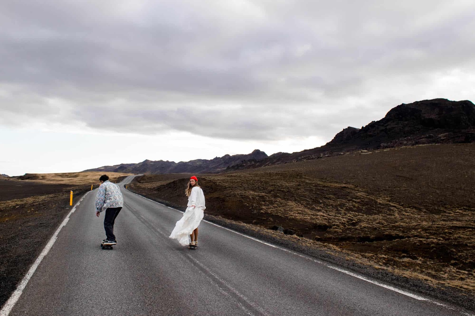 Hochzeitspaar fährt mit dem Skateboard über eine einsame Straße in Island